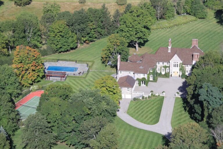 Luxurious estate with expansive grounds, outdoor pool, tennis court, and elegant mansion nestled among lush trees, showcasing premium real estate and lifestyle living.
