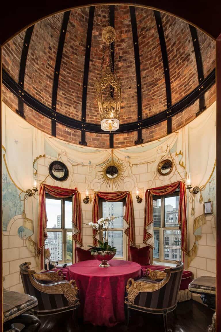 Elegant interior of a room with a round table, plush chairs, ornate drapes, and a dramatic brick vaulted ceiling featuring a beautiful chandelier, showcasing designer decor and classic luxury style.