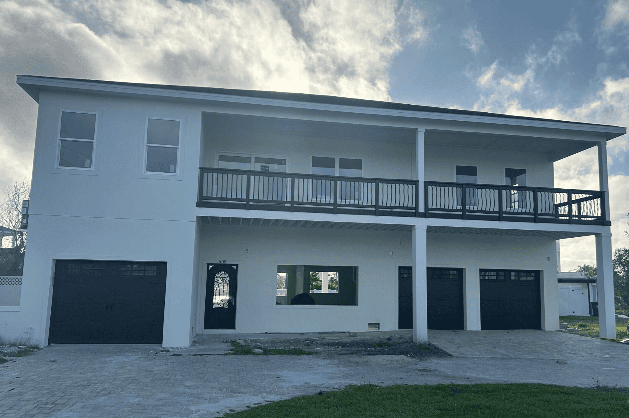 Modern white two-story house with black garage doors and balcony railing, featuring contemporary architecture and outdoor living space.