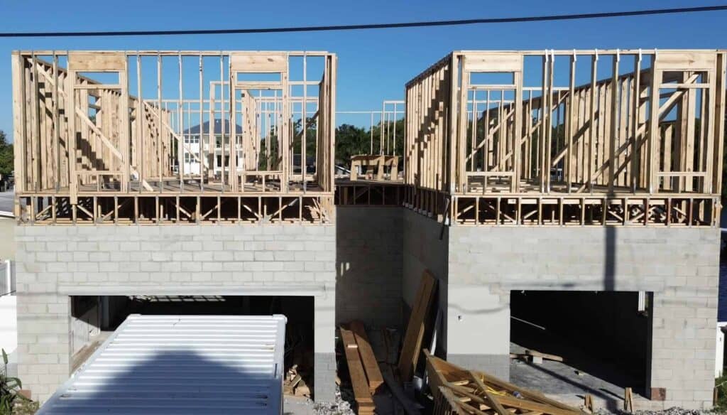 Wooden house framing under construction, featuring a concrete block foundation with vertical wooden studs and roof trusses, highlighting residential building process and construction development.
