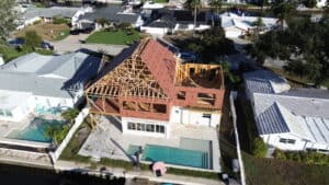 Aerial view of a house under construction showing wooden framework and roofing in a suburban setting with neighboring homes and pools.