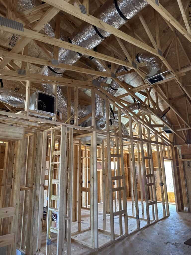 A construction site showcasing wooden framing with electrical wiring and HVAC ductwork installation, highlighting structural development and expertise in building infrastructure.